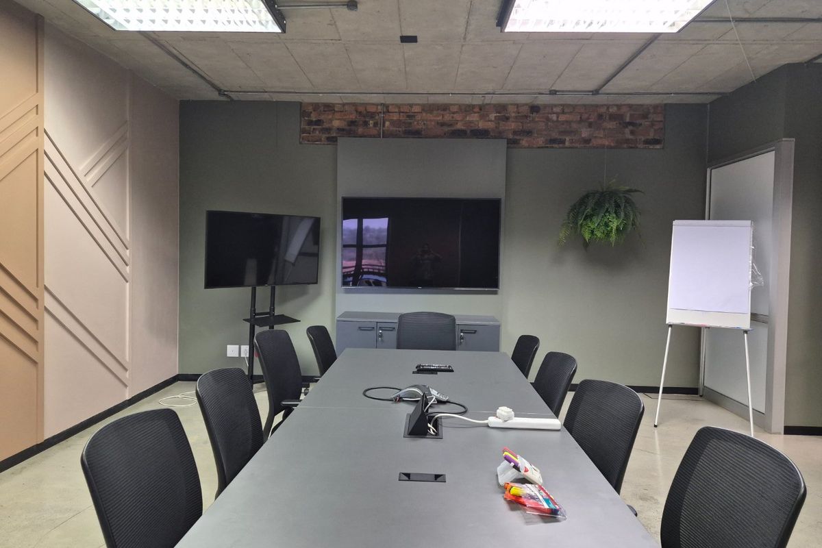 A modern professional boardroom featuring an exposed concrete ceiling, industrial-style lighting, built-in cabinetry, and an exposed brick accent wall.