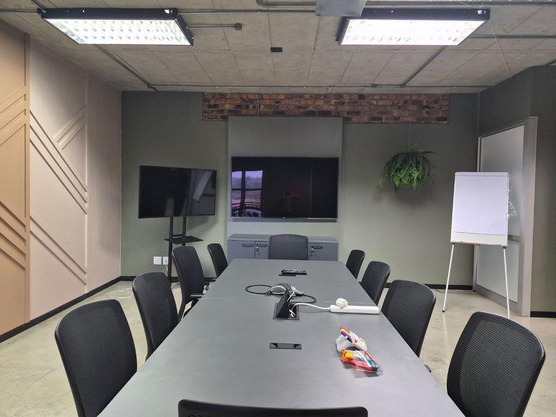 A modern professional boardroom featuring an exposed concrete ceiling, industrial-style lighting, built-in cabinetry, and an exposed brick accent wall.