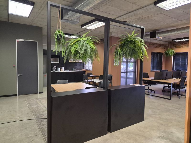 Modern open-plan commercial office space featuring exposed industrial ceilings, polished concrete floors, and a functional kitchenette area with black cabinetry.