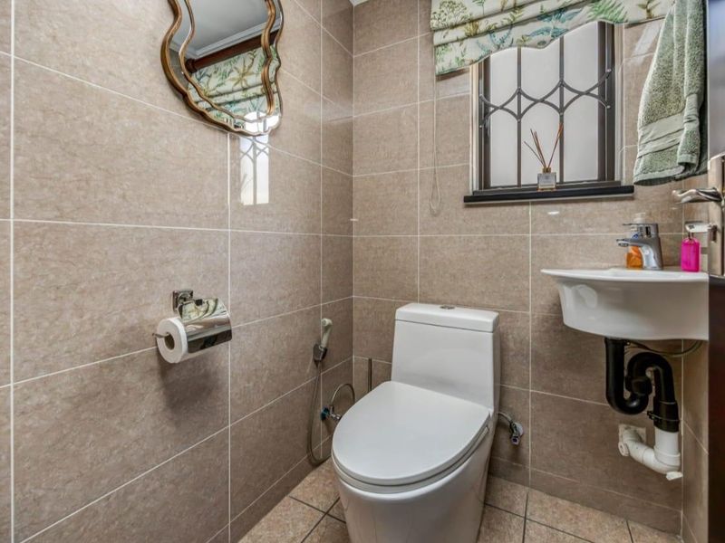 Compact guest bathroom featuring floor-to-ceiling tiling, a modern toilet, and a wall-mounted basin with security bars on the window.