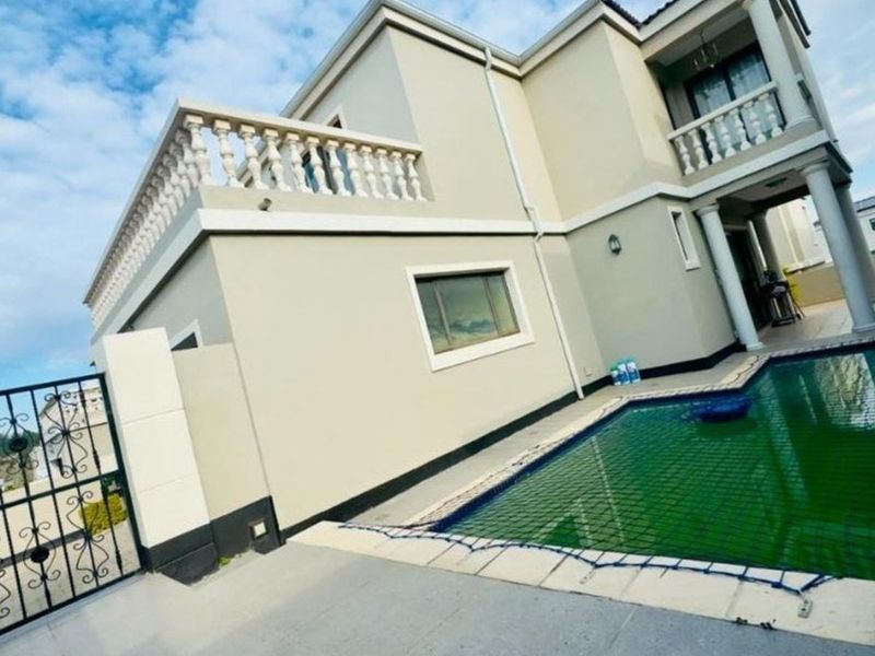 Rear exterior view of a two-story house featuring a swimming pool, tiled patio area, and an upper-level balcony with decorative balustrades.