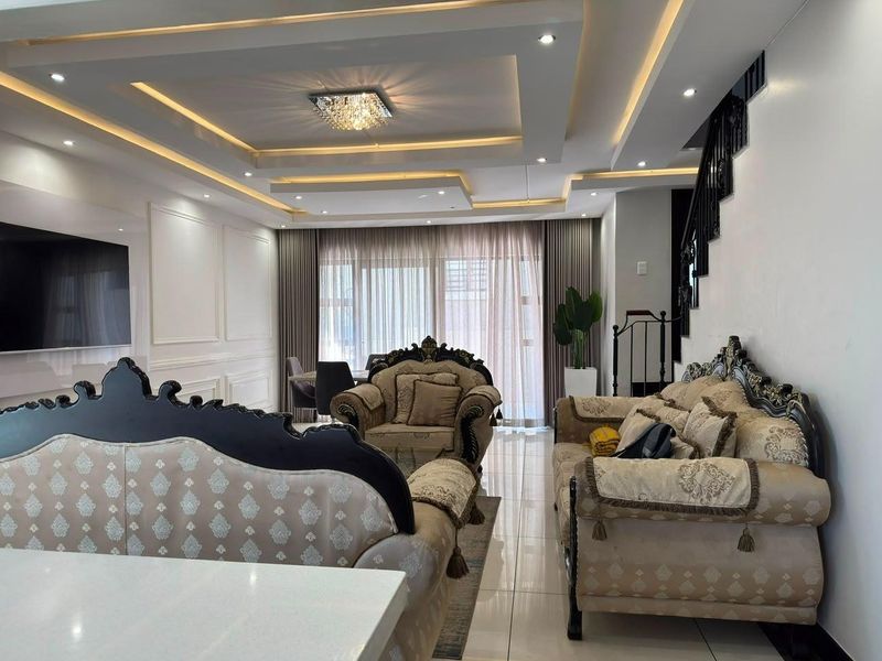 Spacious living area featuring elegant recessed ceilings with cove lighting, wainscoting wall detailing, and polished tiled flooring.
