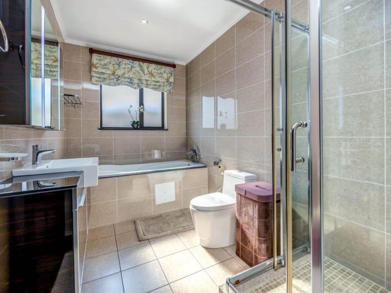 A well-maintained bathroom featuring a built-in vanity, bathtub, separate glass shower enclosure, and neutral floor-to-ceiling tiling.