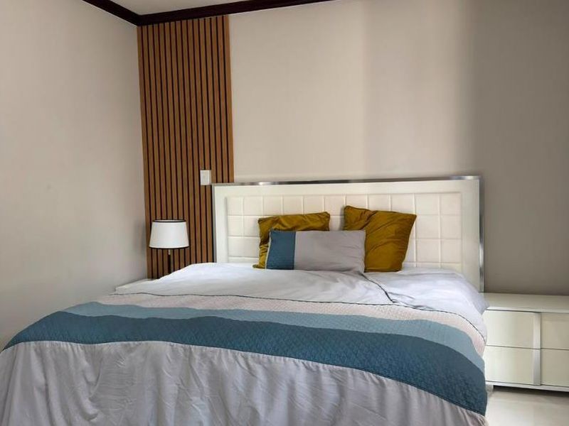 A modern bedroom featuring tiled flooring, recessed downlighting, and a decorative timber slat feature wall behind the bed area.