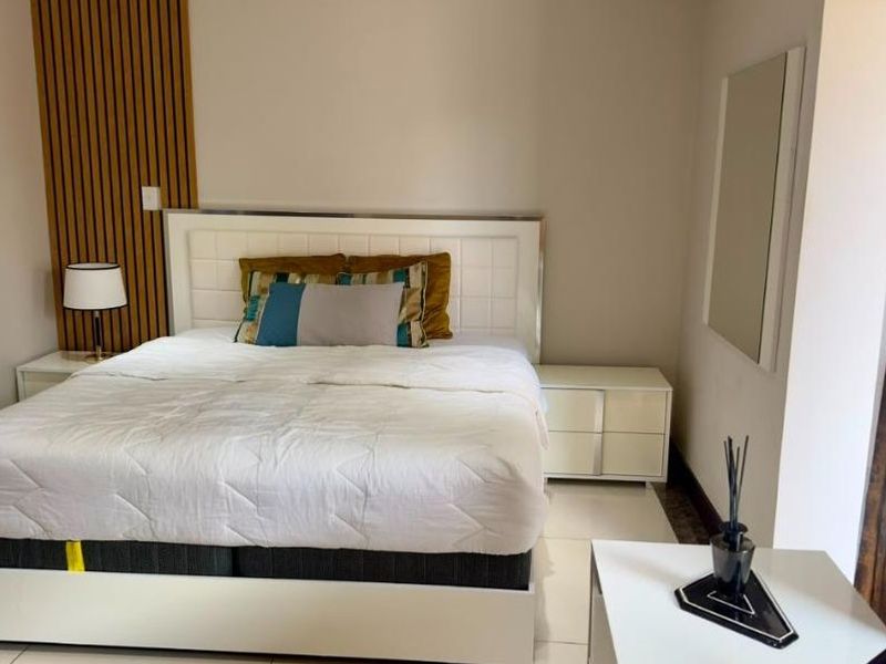 A modern bedroom featuring tiled flooring, recessed downlighting, and a decorative slatted timber feature wall behind the bed area.