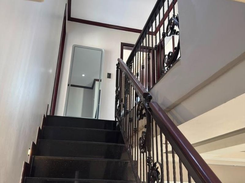 A well-maintained staircase featuring dark stone treads, a decorative wrought iron balustrade, and a polished wooden handrail leading to an upper landing.