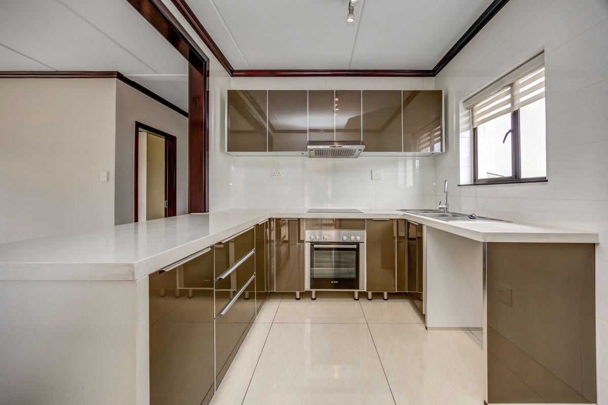 Modern kitchen featuring high-gloss cabinetry, stone countertops, integrated oven and hob, and tiled finishes in a clean, functional layout.