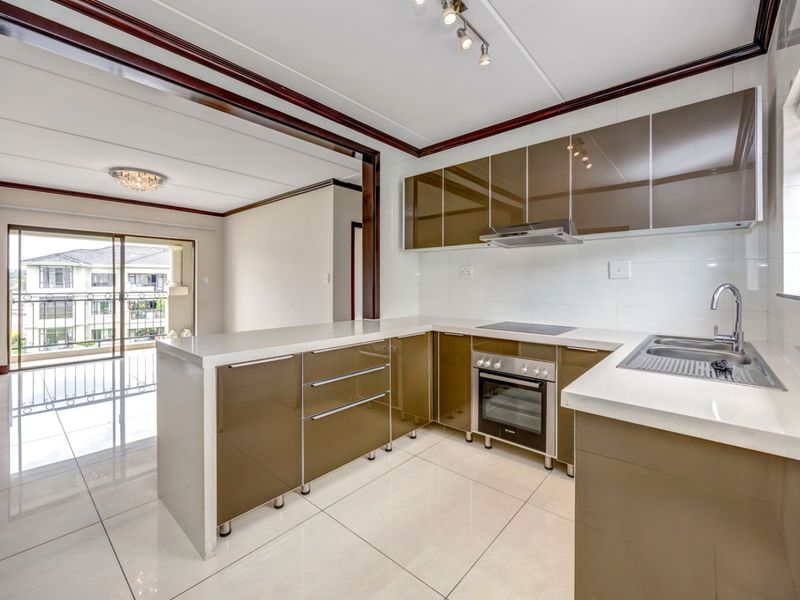 Modern open-plan kitchen featuring glossy cabinetry, stone countertops, and integrated appliances, flowing into a bright living area with access to a balcony.