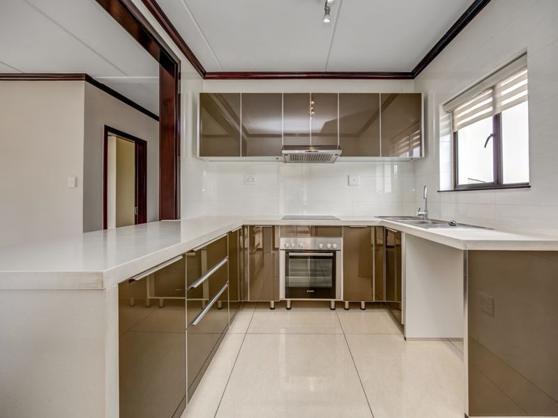 Modern kitchen featuring glossy brown cabinetry, stone countertops, built-in oven, electric hob, extractor fan, and tiled flooring.