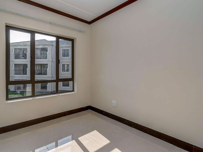 A bright, empty bedroom featuring neutral tiled flooring, dark wood-finish skirting boards, and a large aluminium-framed window.