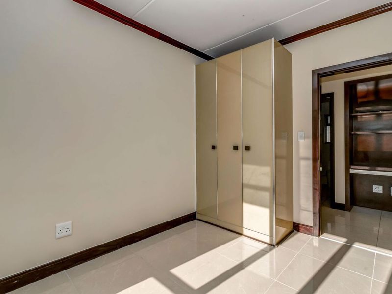 A bright, empty bedroom featuring neutral tiled flooring, a built-in wardrobe, and dark wood trim accents, leading into an adjacent room.