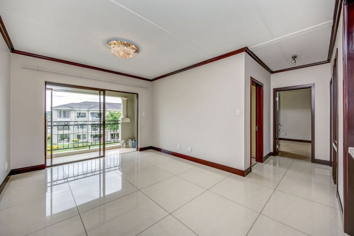 A bright, empty living room featuring polished tile floors, dark wood trim, and a sliding glass door leading to a private balcony.