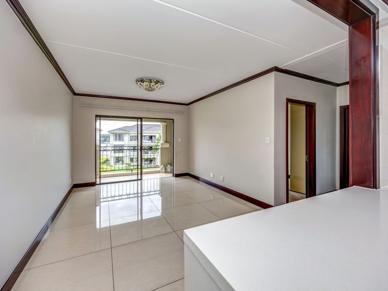 Spacious open-plan living area featuring polished tile flooring, dark wood trim, and direct access to a private balcony through sliding glass doors.