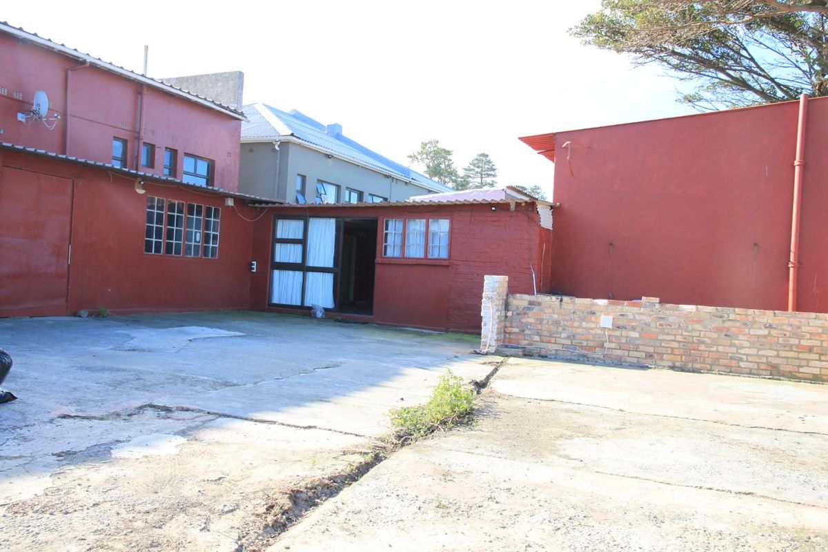 Rear exterior view of the commercial property featuring a concrete courtyard, brick boundary wall, and painted masonry building facade.