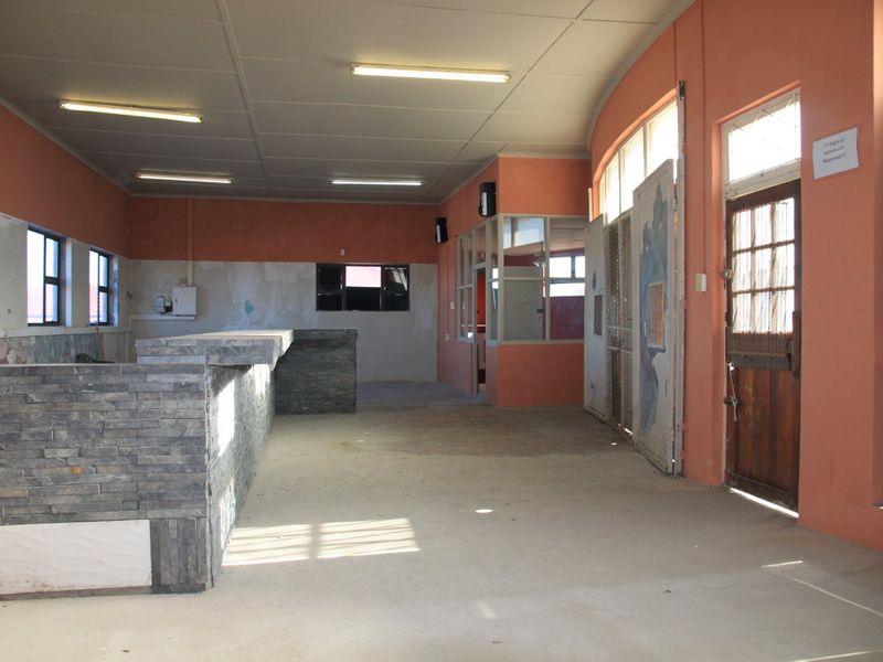 An empty commercial bar area featuring a stone-clad counter, fluorescent lighting, and direct access through a timber-framed door.