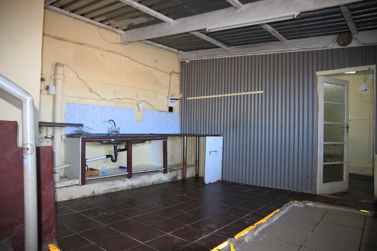 A basic, industrial-style kitchen area featuring a sink, tiled splashback, and exposed structural elements, currently in need of renovation and finishing.