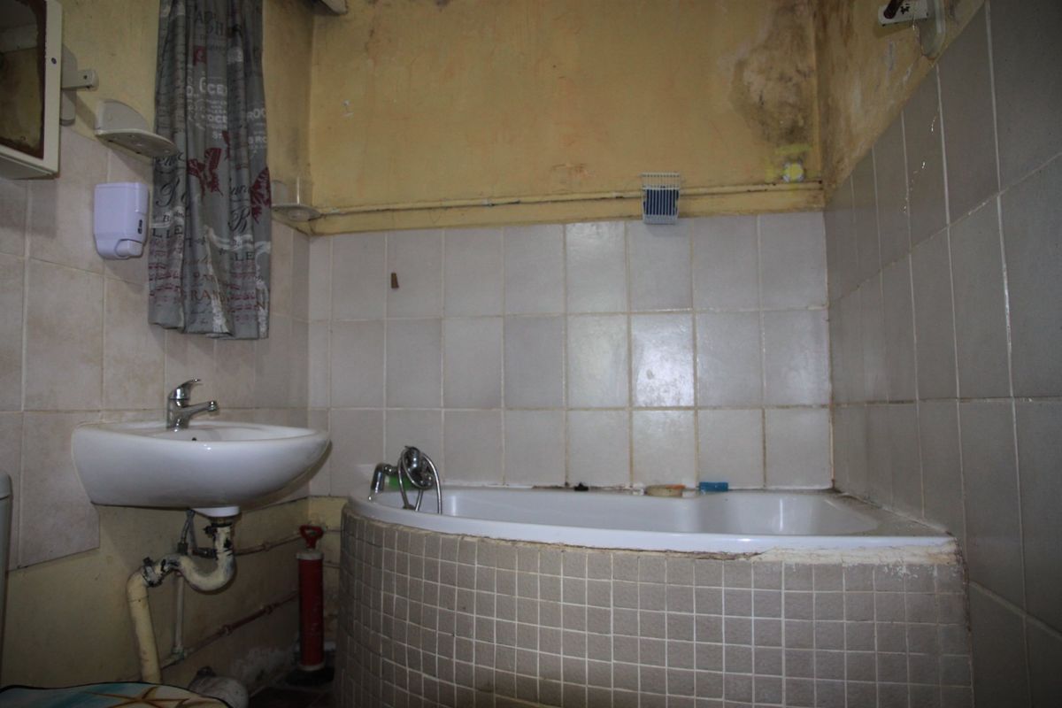 A dated bathroom featuring a built-in bathtub and wall-mounted basin, currently showing significant signs of wear and water damage to the wall finishes.
