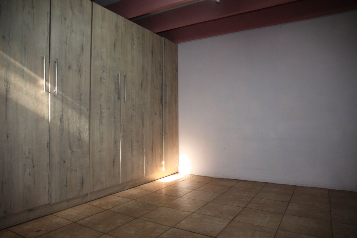 A clean, empty bedroom featuring modern wood-look built-in cupboards, tiled flooring, and exposed ceiling beams, offering a neutral space ready for customization.