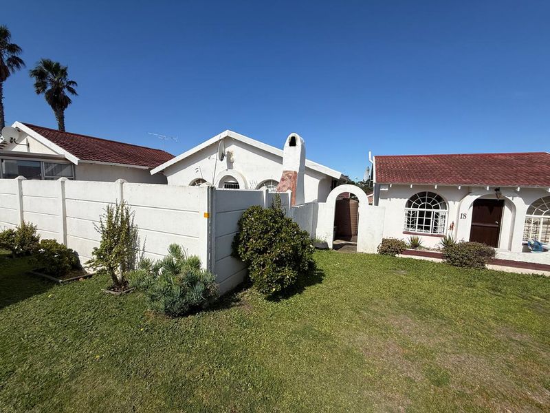 Front exterior view of a townhouse featuring a white facade, tiled roof, arched windows, and a private front garden with a boundary wall.