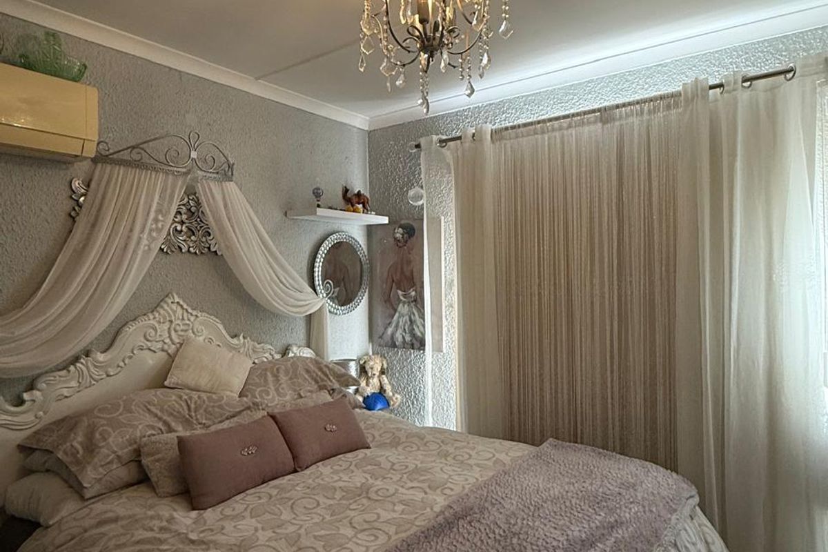 A cozy bedroom featuring textured wall finishes, a central crystal chandelier, and a wall-mounted air conditioning unit with floor-to-ceiling window treatments.
