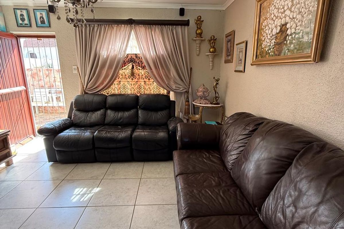 A living room featuring tiled flooring, a decorative ceiling rose with a chandelier, and direct access to an outdoor area via a security gate.