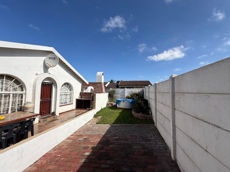 Rear exterior view of the townhouse featuring a paved patio, built-in braai area, small lawn, and high precast concrete boundary walls.