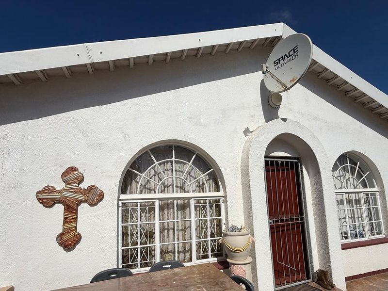 Exterior view of a townhouse featuring arched windows, a security gate, and a white stucco facade with a mounted satellite dish.