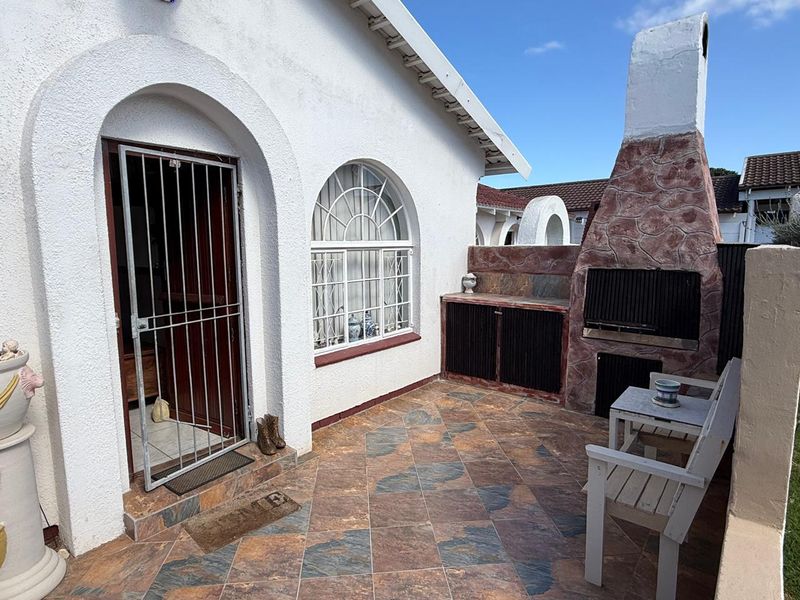 Outdoor patio area featuring a built-in braai with stone cladding, tiled flooring, and an arched entrance with a security gate.