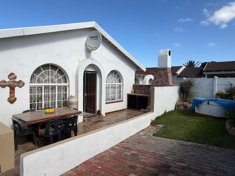 Rear exterior view of the townhouse featuring a tiled patio, built-in braai, brick paved area, and arched windows.