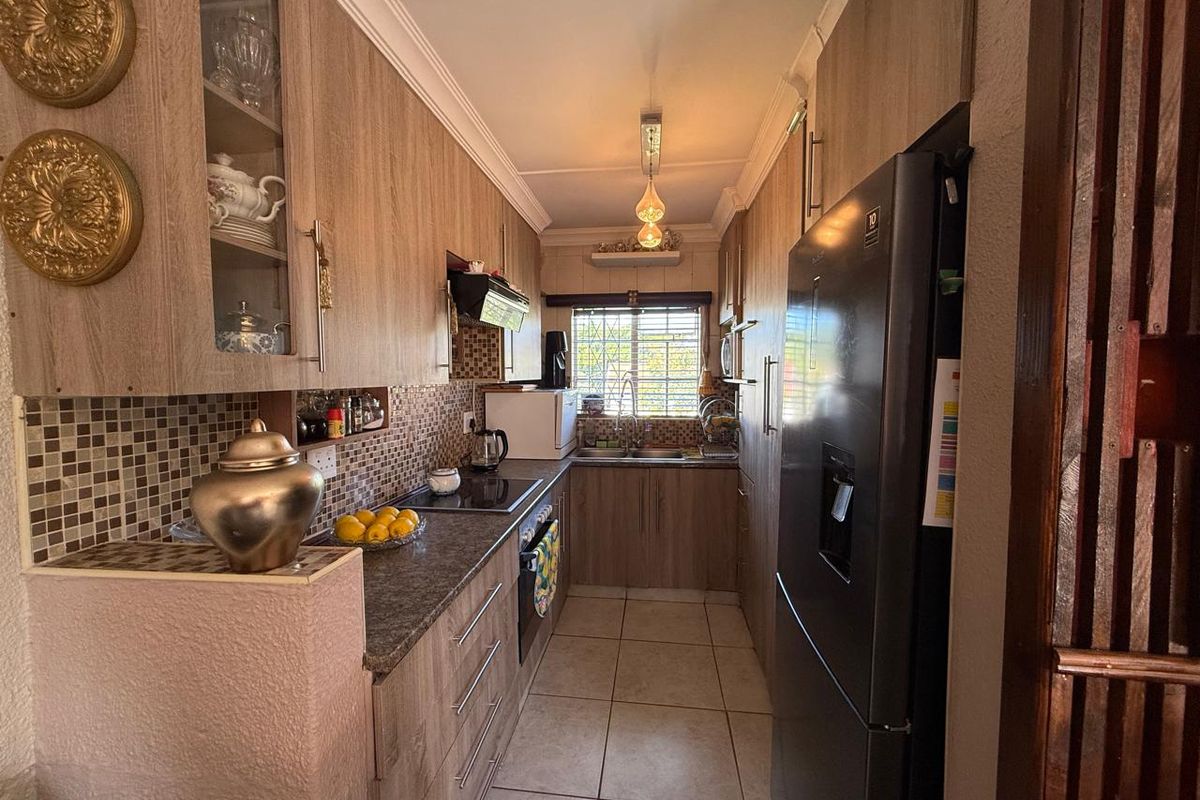 A functional galley-style kitchen featuring wood-look cabinetry, mosaic tile backsplash, ceramic floor tiles, and integrated cooking appliances.