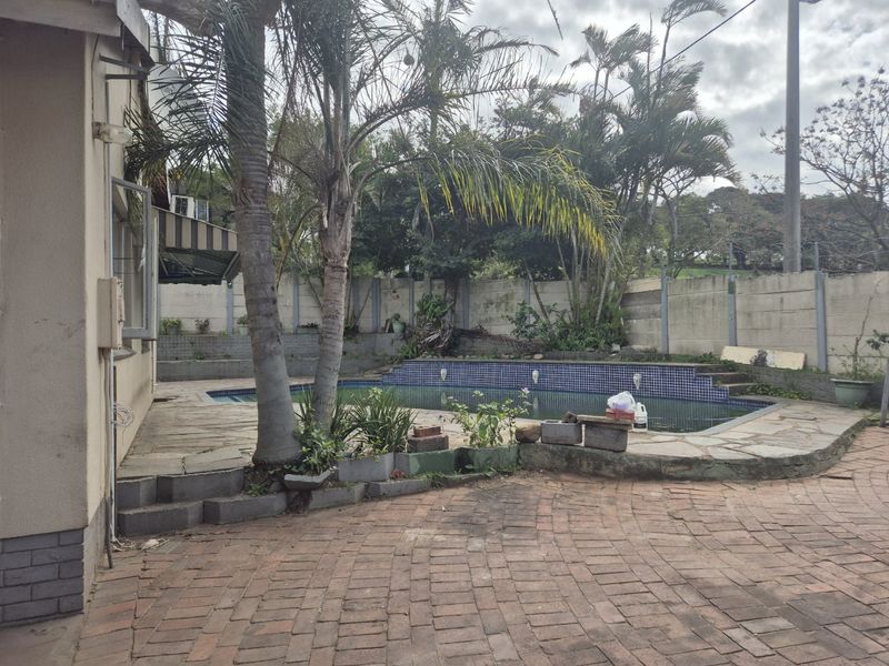 Outdoor pool area featuring a tiled swimming pool, brick paved patio, and perimeter boundary wall, requiring maintenance and landscaping updates.