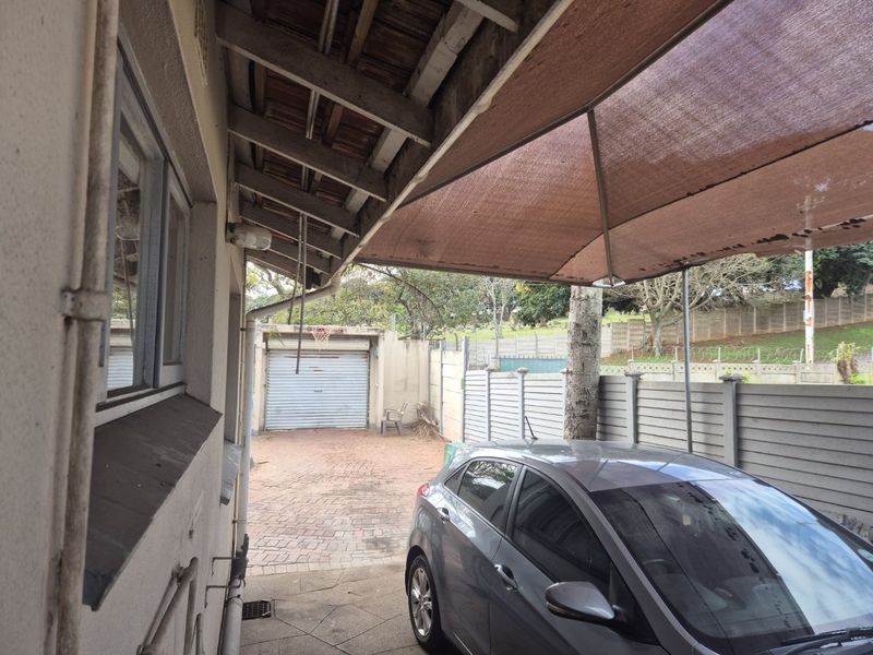 Rear exterior area featuring a paved driveway, a detached garage, and a covered carport structure with weathered timber rafters.