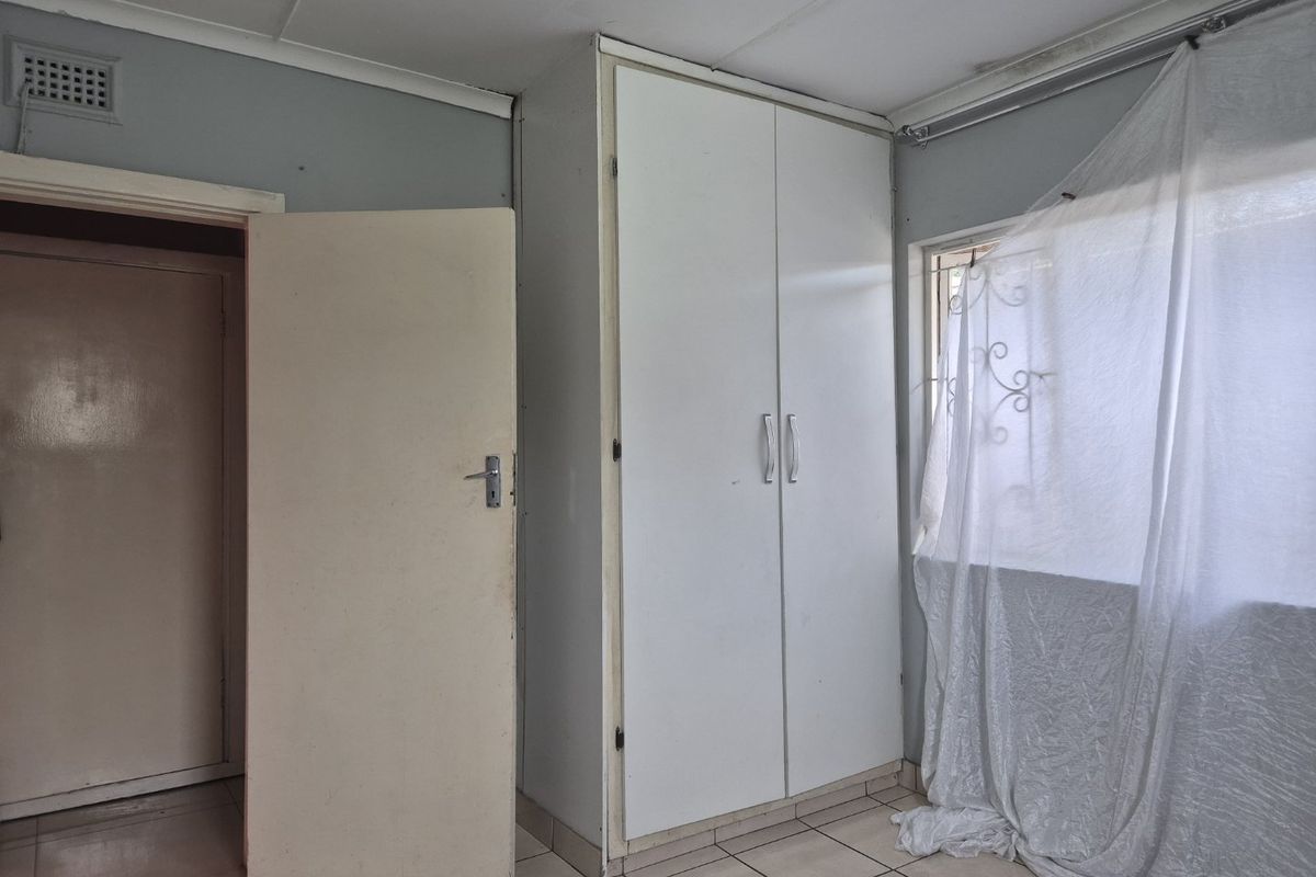 A bedroom featuring tiled flooring and a built-in wardrobe, showing signs of ceiling water damage and general wear requiring maintenance.