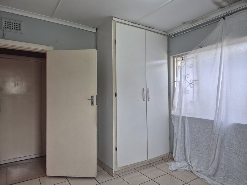 A bedroom featuring tiled flooring and a built-in wardrobe, showing signs of ceiling water damage and general wear requiring maintenance.