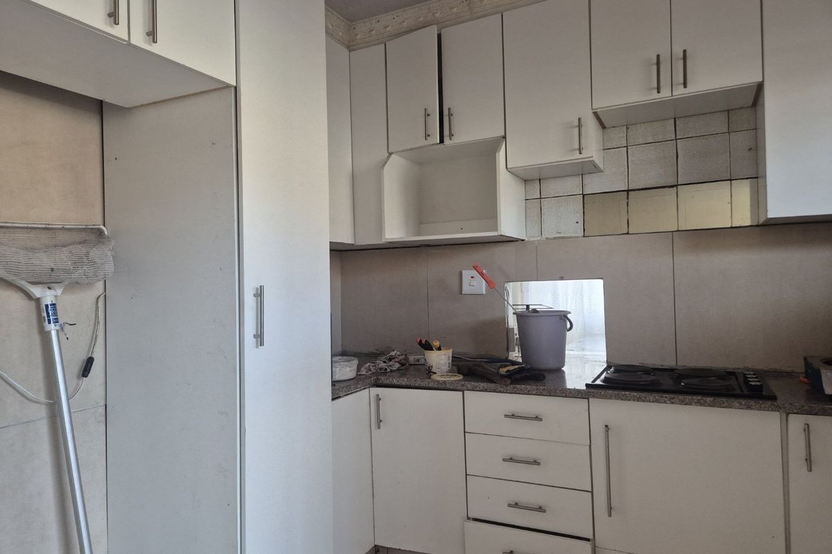 A compact kitchen featuring white built-in cabinetry, granite countertops, and a gas hob, currently requiring minor repairs and cosmetic updates.