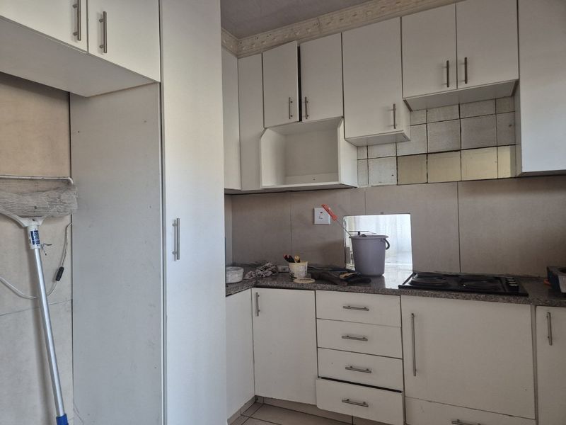 A compact kitchen featuring white built-in cabinetry, granite countertops, and a gas hob, currently requiring minor repairs and cosmetic updates.