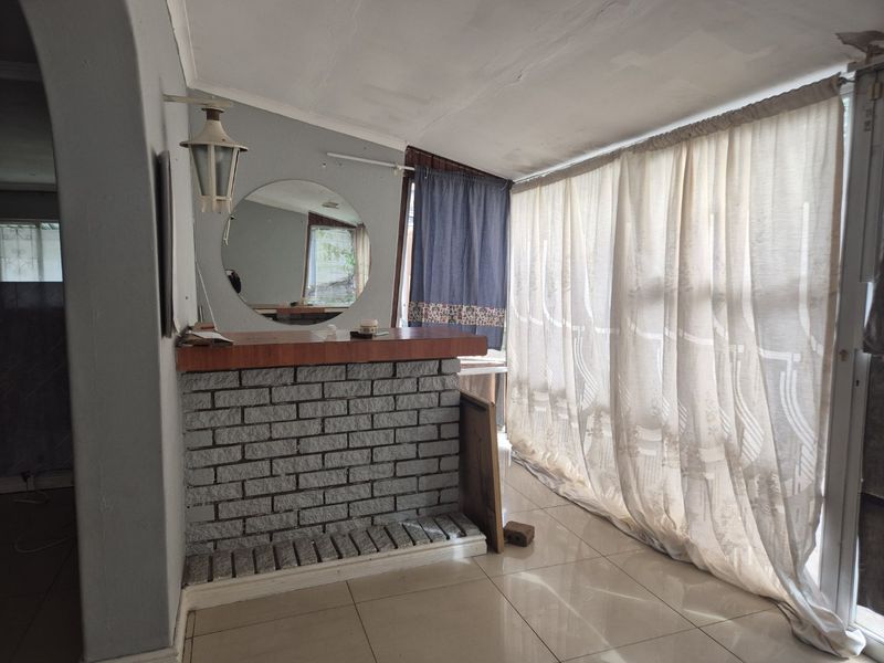 A dated indoor bar area featuring a brick counter, tiled flooring, and a circular mirror, offering potential for a modern entertainment space renovation.