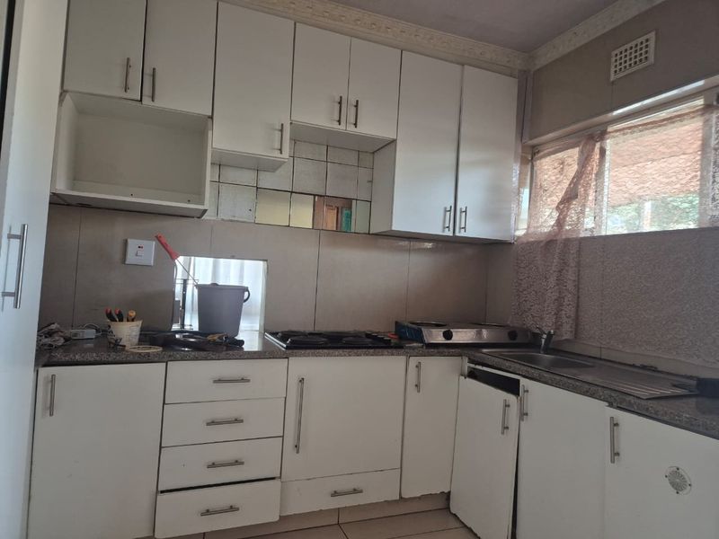 A functional kitchen featuring white cabinetry, granite countertops, and a built-in hob, requiring some maintenance and cosmetic updates to restore its appeal.