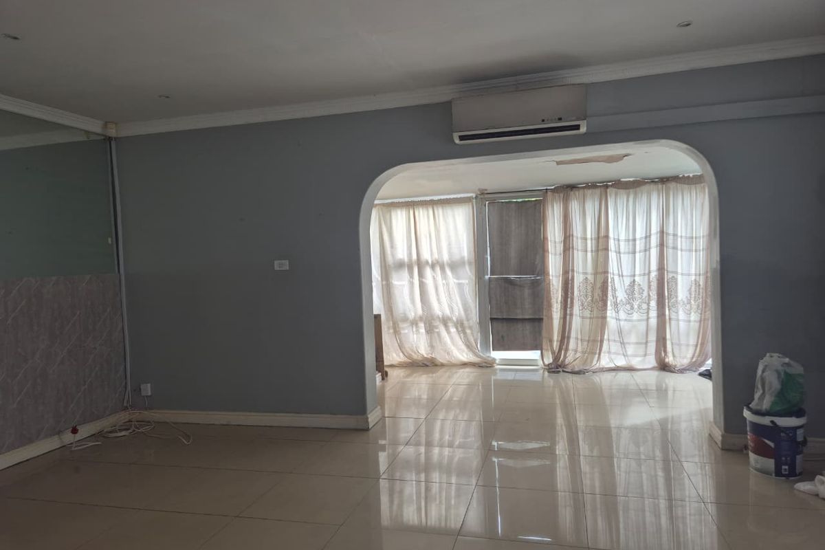 An empty living room featuring tiled flooring, a wall-mounted air conditioning unit, and an arched transition to an adjacent space.