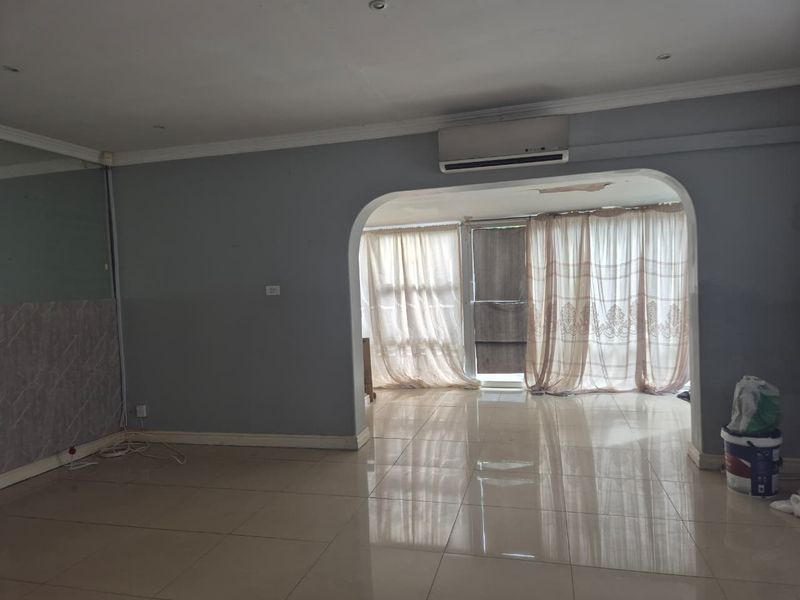 An empty living room featuring tiled flooring, a wall-mounted air conditioning unit, and an arched transition to an adjacent space.