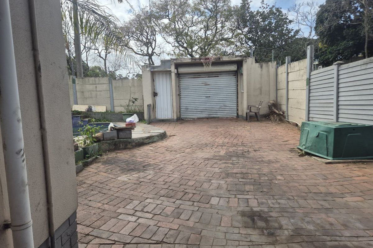 Rear exterior area featuring a brick-paved courtyard, a single garage with a roller shutter door, and a swimming pool enclosed by boundary walls.
