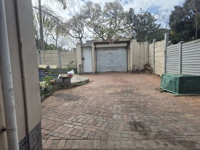 Rear exterior area featuring a brick-paved courtyard, a single garage with a roller shutter door, and a swimming pool enclosed by boundary walls.
