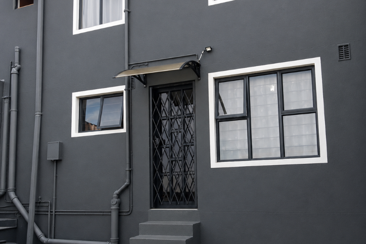 Rear exterior view of the property featuring dark grey plastered walls, aluminium window frames, a security gate, and concrete stairs leading to the entrance.
