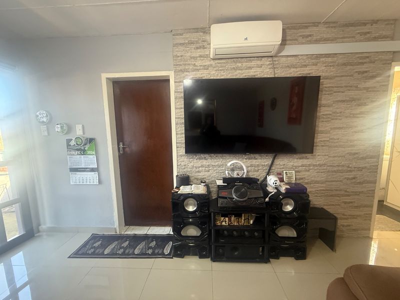 Living room featuring a stone-cladding accent wall, split-system air conditioning unit, and tiled flooring.