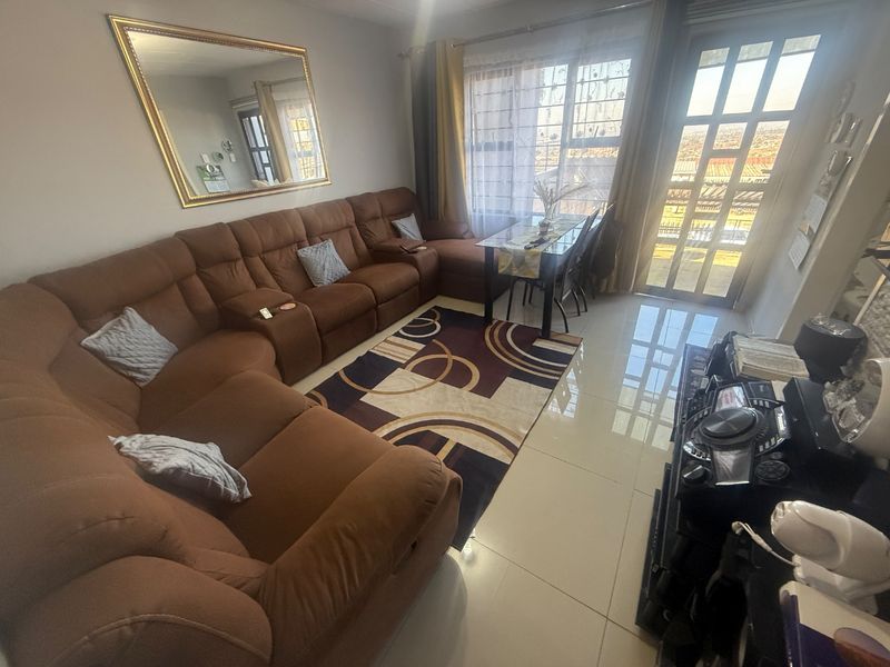A living room featuring tiled flooring, a large window, and a sliding glass door providing access to the exterior.