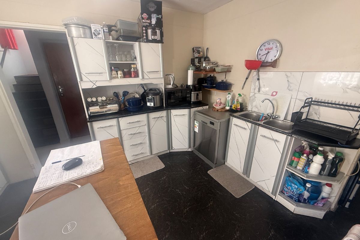 A functional kitchen featuring white cabinetry with marble-effect detailing, dark flooring, tiled splashbacks, and a double bowl sink with integrated dishwasher.
