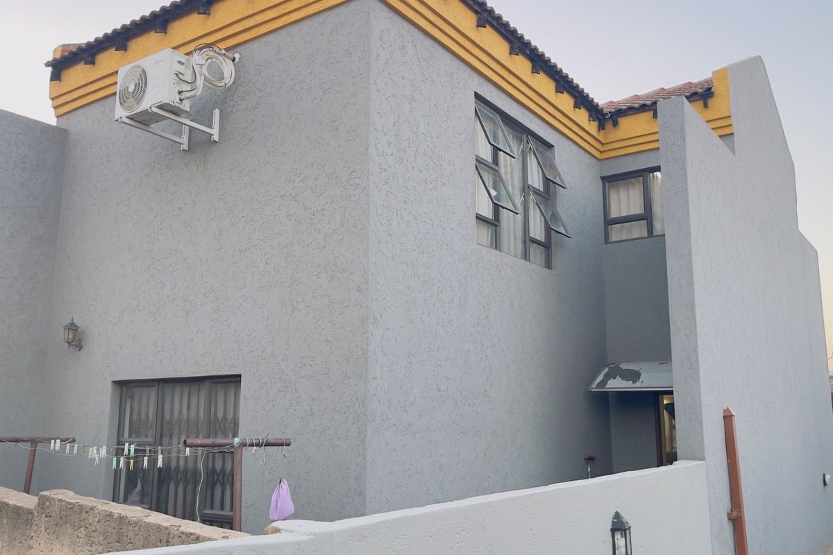 Rear exterior view of a two-story house featuring grey textured walls, casement windows, and an external air conditioning unit.