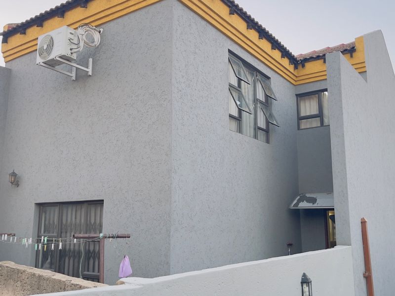 Rear exterior view of a two-story house featuring grey textured walls, casement windows, and an external air conditioning unit.