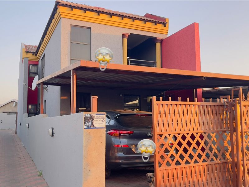 Front exterior view of a two-story house featuring a carport, metal gate, boundary wall, and an upper-level balcony.