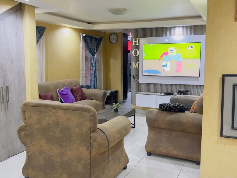 A cozy living room featuring a modern built-in media wall, tiled flooring, and recessed ceiling details, providing a comfortable space for relaxation.